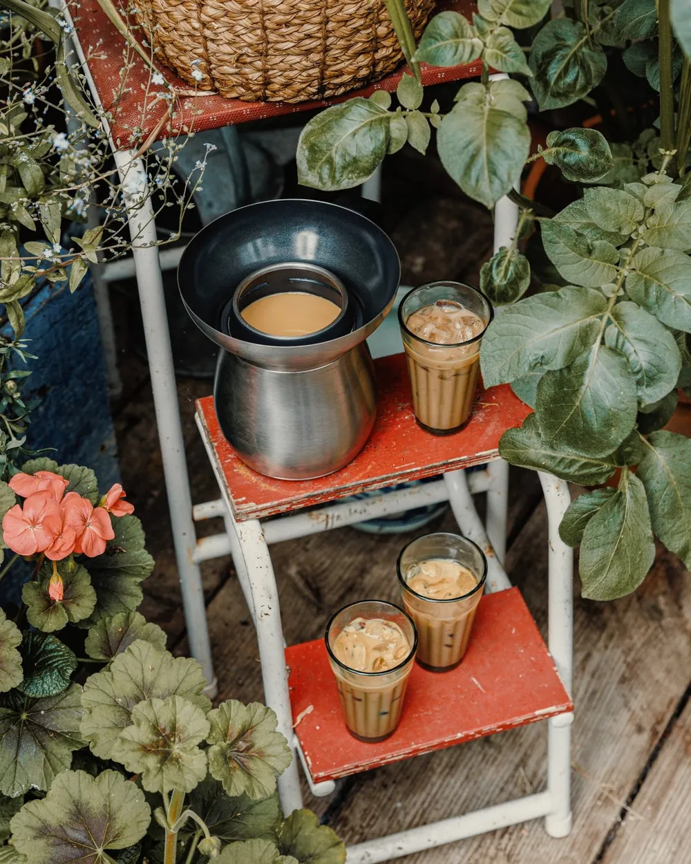 The Chai Maker and two glasses of chai on a red plant stand among leaves