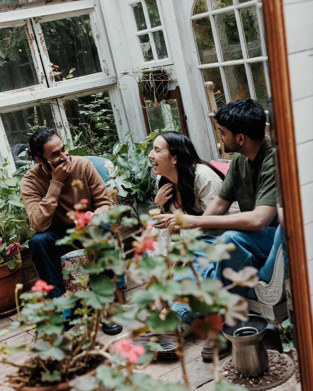 Friends sharing glasses of chai around a table in a sunny room full of plants